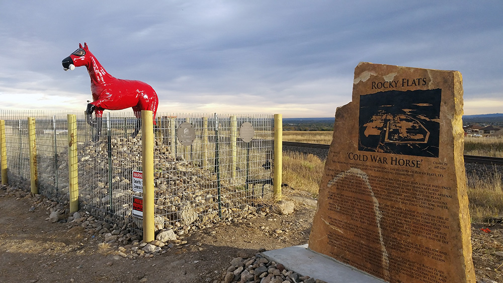 Statue of a horse in a gas mask and red full-body suit is knocked over and sits on the ground